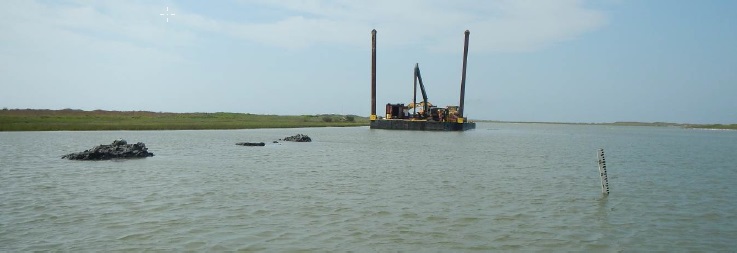 Excavator digging floatation channel within the dredge template for barge access, sidecast material in foreground